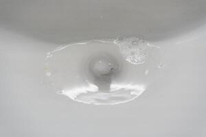 White ceramic bathroom sink with water that goes down the drain. With space to copy photo