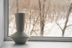 A single empty vase stands on the windowsill against the background of a frozen window in winter. The concept of frost and cold weather. photo