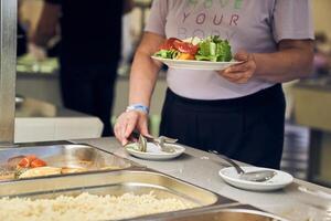 A woman serves a salad of fresh vegetables. Buffet service at the hotel. Offering self-service options, ideal for creating a copyspace image. photo