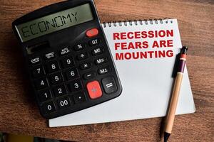 Concept of Recession Fears are Mounting write on sticky notes and Economy text in calculator isolated on Wooden Table. photo