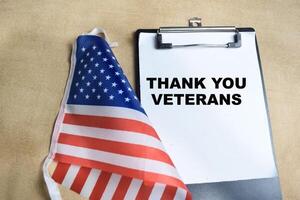 Concept of Thank you Veterans write on paperwork with the united states flag isolated on Wooden Table. photo