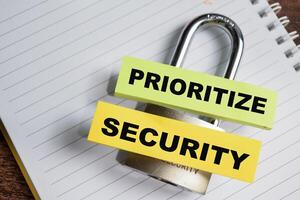 Concept of Prioritize Security write on sticky notes and padlock isolated on Wooden Table. photo