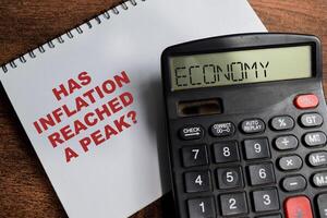 Concept of Has Inflation Reached a Peak write on sticky notes and Economy text in calculator isolated on Wooden Table. photo