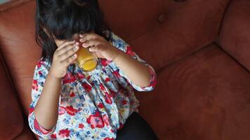 Young child enjoys juice while sitting on a cozy brown couch video