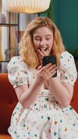 Happy redhead woman at home use smartphone typing browsing wow yes found out great big win celebrate video