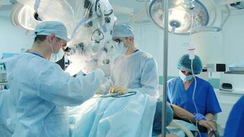 Team of surgeons conducting a precise operation with the assistance of an electron microscope in a sterile operating room. Advanced medical technology used for intricate procedures. video