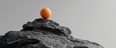 The image shows a black and orange ball sitting on top of a rock. photo
