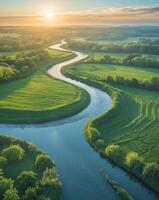 Serene aerial view of a meandering river flowing through lush green fields under a clear blue sky at sunrise photo