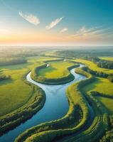 Serene aerial view of a meandering river flowing through lush green fields under a clear blue sky at sunrise. photo