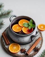 A Cozy Pot of Mulled Wine with Orange Slices and Mint Garnish Surrounded by Spices and Evergreen on a Rustic Wooden Coaster for Winter Warmth. photo