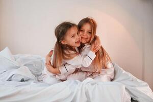 Embracing each ,other on the bed. Two little girls are playing and having fun together in domestic room photo