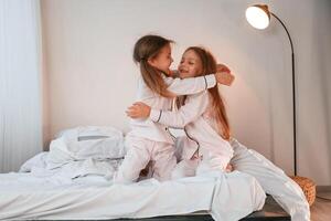 Embracing each other on the bed. Two little ,girls, are playing and having fun together in domestic room photo