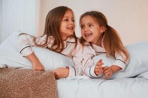 Smiling, laying, down on the bed. Two little girls are playing and having fun together in domestic room photo