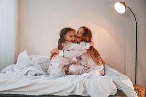 Embracing, each other on the bed. Two little girls are playing and having fun together in domestic room photo