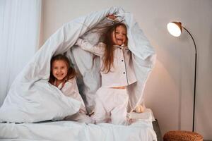 In the bedroom, with blanket in hands. Two little girls are playing and having fun together in domestic room photo