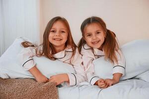 Smiling,, laying down on the bed. Two little girls are playing and having fun together in domestic room photo