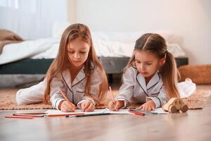 Two, little girls, are lying down on the ground and drawing together in domestic room photo