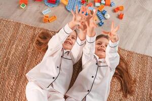 With hands up.. Lying down on the floor. Two little girls are playing and having fun together in domestic room photo