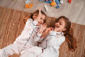 Top, view. Lying down. Construction plastic toys. Two little girls are playing and having fun together in domestic room photo