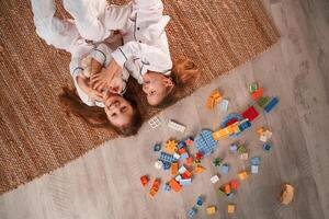 Top view. .Lying down.. Construction plastic toys. Two little girls are playing and having fun together in domestic room photo