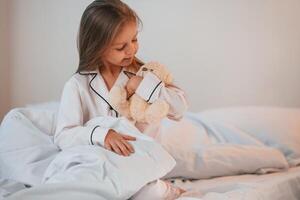 Little girl, with, teddy bear in hands is sitting on the bed at home photo