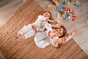 Top view.. Lying down. Construction plastic toys. Two little girls are playing and having fun together in domestic room photo