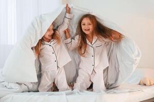 Under the blanket on bed. Two little girls are playing and having fun together in domestic room photo