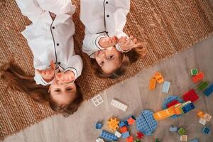 With hands up. Lying down on the floor. Two little girls are playing and having fun together in domestic room photo