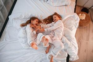 Tickling each ,other on the bed. Two little girls are playing and having fun together in domestic room photo
