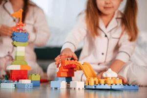 Bunch of plastic, construction, toys are on the floor. Two little girls are playing and having fun together in domestic room photo