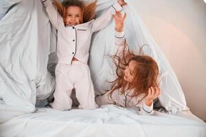 Holding ,the, blanket. Two little girls are playing and having fun together in domestic room photo