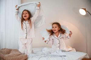 Active ,weekend. On the bed with pillows. Two little girls are playing and having fun together in domestic room photo