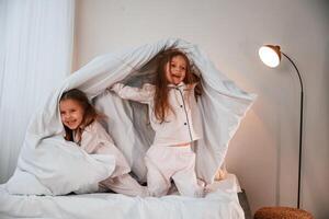 In the bedroom ,with blanket in hands. Two little girls are playing and having fun together in domestic room photo