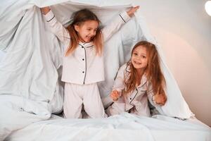 Holding the blanket.. Two, little girls are playing and having fun together in domestic room photo