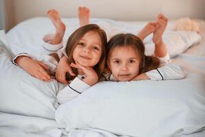 Smiling, laying down on the bed.. Two little girls are playing and having fun together in domestic room photo