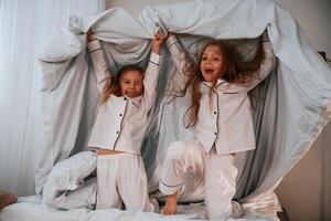 In, the bedroom, with blanket in hands. Two little girls are playing and having fun together in domestic room photo