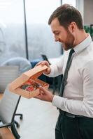 Man in white shirt and tie is standing, in the office and holding Christmas type of gifts in the paper eco boxes photo