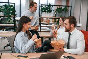 Casual conversation. Group of, coworkers are eating food from eco boxes in the office together photo