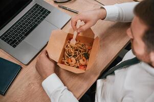 Top view. Businessman in formal clothes is in the office eating udon that is in the eco box photo