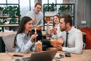 Having, a conversation. Group of coworkers are eating food from eco boxes in the office together photo