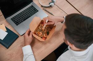 Top, view. Businessman in formal clothes is in the office eating udon that is in the eco box photo