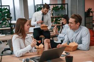 Talking, having, a break.. Group of coworkers are eating food from eco boxes in the office together photo