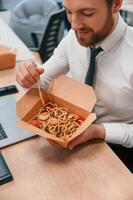 Businessman ,in formal, clothes is in the office eating udon that is in the eco box photo