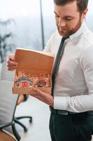 Man in white shirt and tie is ,standing, in the office and holding Christmas type of gifts in the paper eco boxes photo