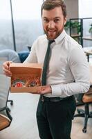 Man in white shirt and tie is standing in the office and holding Christmas type of gifts in the paper eco boxes photo