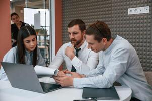 Sitting, talking, using laptop. Office ,workers are indoors by the table photo
