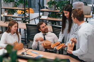 Having a conversation. Group of coworkers are eating food from eco boxes in the office together photo