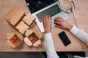 Top view ,of man's hands that is typing on the laptop. Food in the paper eco boxes are on the table photo
