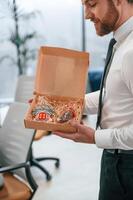Man in white shirt ,and tie is standing in the office and holding Christmas type of gifts in the paper eco boxes photo
