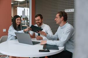Sitting, talking, using laptop. Office workers are indoors b.y the table photo